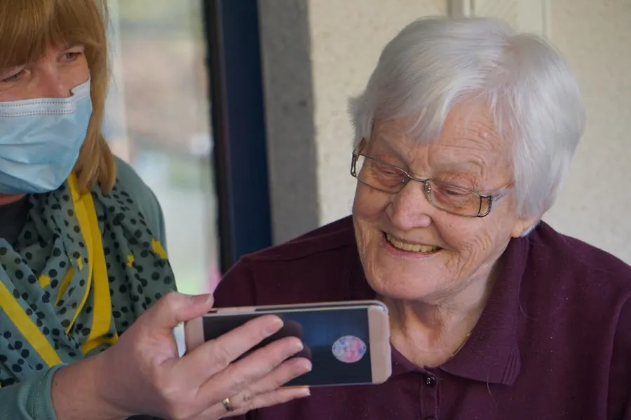 A carer showing a resident something on a phone, both smiling