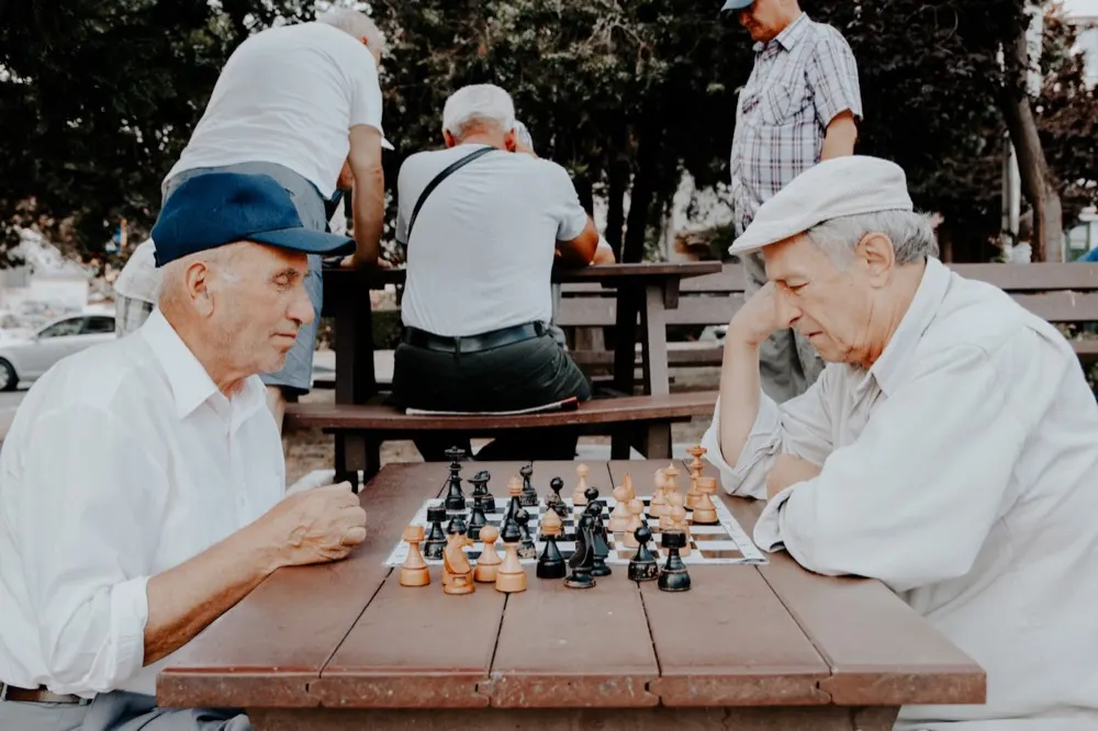 Two older men playing chess at an outdoor table