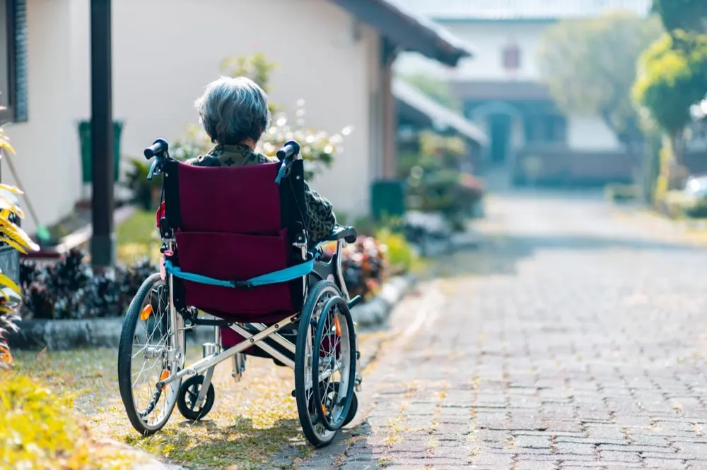 A person in a wheelchair on a paved garden path outside a home