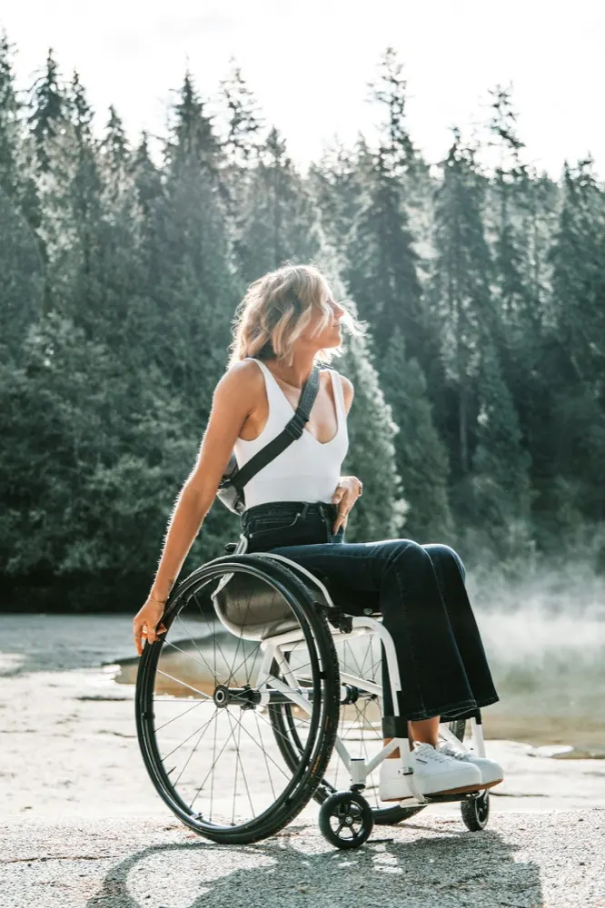 A woman in a wheelchair outdoors beside a lake
